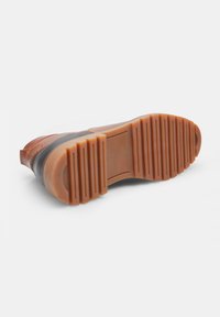 Suola in gomma marrone con scanalature, caratterizzata da un sopra nero slanciato. Il design è lineare con una finitura liscia e dettagli minimi.