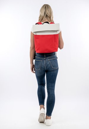 Rucksack mit rotem und weißem Rollverschluss, glatter Textur und verstellbaren schwarzen Trägern. Er besticht durch ein minimalistisches Design ohne sichtbare Beschläge.