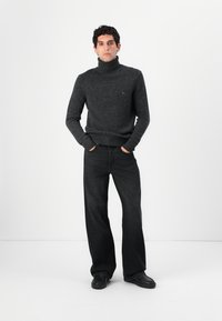 Temno siva pletena turtleneck pulover in črne široke hlače z gladko teksturo. Obleka je dopolnjena s črnimi čevlji.