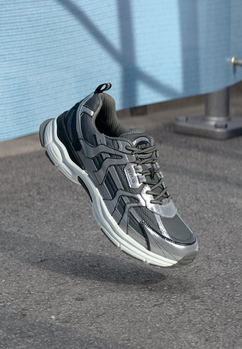 Chaussures de sport grises avec tige en mesh et synthétique, col rembourré et design à lacets. Comprend une semelle intermédiaire blanche épaisse et des accents texturés.
