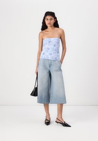 Top azzurro chiaro senza spalline con motivo floreale, abbinato a culotte in denim azzurro chiaro con gamba ampia. Scarpe slingback nere con punta affusolata e borsa.