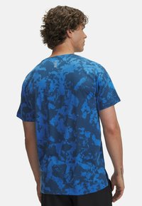 Camiseta de manga corta en diferentes tonos de azul con un patrón abstracto y tejido texturizado; presenta un diseño único en la parte posterior con cinco acentos verticales.