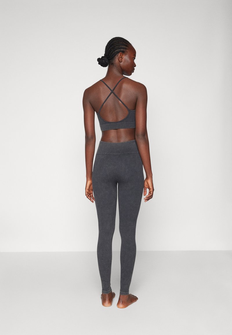 Dunkelgrauer, gerippter Sport-BH mit überkreuzten Rückenträgern, kombiniert mit passenden, gerippten Leggings mit hohem Bund, barfuß sichtbar.