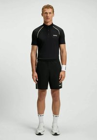 Camisa polo preta de mangas curtas, com detalhes brancos e o logotipo "BOSS". Combinada com calções pretos e ténis brancos com meias estampadas.