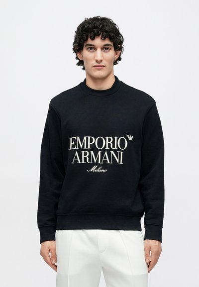 Czarna bluza bawełniana z okrągłym dekoltem. Na przodzie znajduje się duży biały napis "EMPORIO ARMANI Milano".