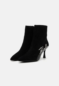 Zwarte suède enkellaarsjes met puntige neuzen en een stilettohak van 10 cm. Kenmerkt zich door een zilveren "Karl" handtekeningdetail aan de zijkant.