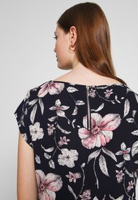 Crop top com padrão floral apresentando flores rosa e brancas sobre um fundo azul-marinho, com um fecho de correr visível na parte de trás e mangas em forma de ombro.