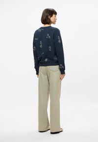 Μπλούζα navy με εκτυπώσεις μπροστά και πίσω, διαθέτει σχέδια φυτών και ζώων σε μπεζ απόχρωση. Συνδυάζεται με ανοιχτό μπεζ παντελόνι καμπάνα.