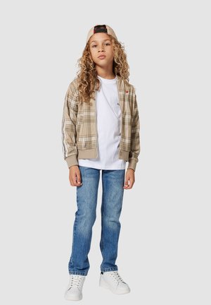 Beige plaid bomber jacket with zipper, white t-shirt, blue jeans, and white sneakers. Light tan cap completes the outfit.