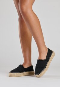 Zwarte canvas espadrille slippers met gescheurde randen, geweven jute zolen en contrasterende stiksels. Laag profiel ontwerp, geschikt voor casual gebruik.