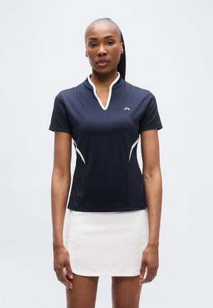 Πόλο μπλούζα ναυτικού μπλε με κοντά μανίκια και λευκή λεπτομέρεια γιακά· συνδυασμένη με εφαρμοστή λευκή φούστα. Λείο ύφασμα, κομψός σχεδιασμός.