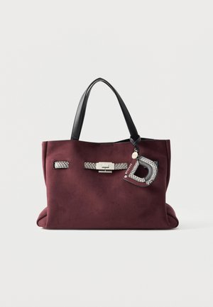 Vinrød ruskinds-tote taske med sorte håndtag, sølvspænde, vævede detaljer og en tekstureret bogstav D-nøglering, der hænger fra det ene håndtag.