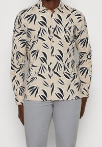 Camisa de manga larga en beige claro con un estampado de hojas en blanco y negro. Cuello abotonado, cierre de botones en el frente y diseño de corte slim.