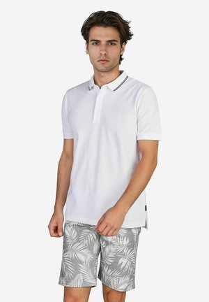 Witte polo met een kraag en twee knopen, met een marineblauw gestreepte rand. Gecombineerd met grijze shorts met een wit bladerenpatroon.