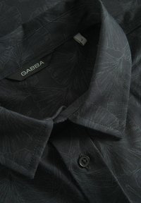 Cămașă neagră cu mânecă scurtă, cu un model floral subtil, dotată cu guler tip button-down, eticheta GABBA și un detaliu cu un singur buton negru.