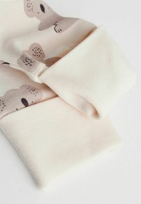 Blødt bomuldsstof i lyserød med bjørnemønstre. Har rullede manchetter og en glat tekstur. Designet til komfort og slidstyrke.