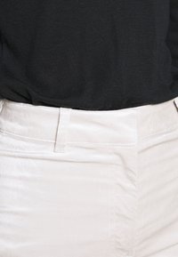 Pantalon en coton de couleur claire avec une texture lisse ; doté d'un design à l'avant plat, de passants de ceinture et d'un éclat subtil.