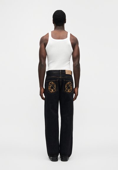 Τζιν με σκουρόχρωμο ξέβγαλμα και σχέδια αστροναυτών στις πίσω τσέπες, συνδυ ασμένα με λευκή φανέλα. Η εφαρμογή είναι χαλαρή και ίσια.