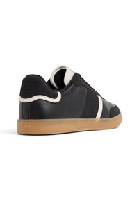 Sneaker nera con tomaia in pelle liscia, dettagli bianchi e suola in gomma color cuoio. Presenta pannelli texturizzati e dettagli cuciti sul retro.