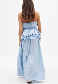 Abito senza spalline di colore blu chiaro con vita a peplum arricciato, gonna fluida e tessuto morbido. La vista posteriore mostra il design a lunghezza completa.