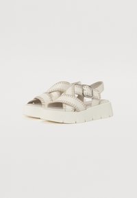 Beige sandaler med kryssede stropper, syddetailer og spenne. Har en tykk hvit plattformsåle og en åpen tådesign.