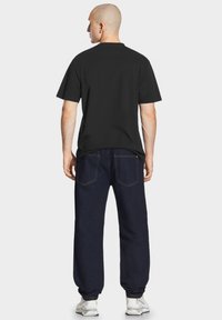 Czarny bawełniany t-shirt z krótkimi rękawami, zestawiony z ciemnoniebieskimi spodniami jeansowymi. Materiał o fakturze i prosty fason z widocznymi detalami przeszyć.