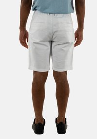 Witte katoenen shorts met een relaxte pasvorm, een elastische tailleband en twee achterzakken, gecombineerd met zwarte sneakers op een neutrale achtergrond.