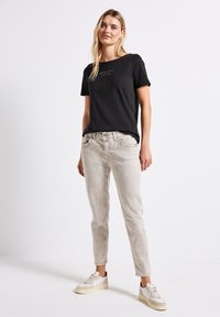 Svart t-shirt med kort ärm och vit text, tillsammans med ljusgrå jeans och vita sneakers med beige detaljer. En enkel, avslappnad outfit.