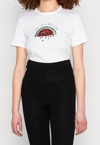 Vit bomull t-shirt med en vattenmelon grafik som har röda paljetter och gröna akcentuer. Matchad med texturerade svarta högmidjade byxor.