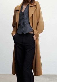 Tan belted trench coat with a collar, paired with a gray buttoned vest and black trousers. Smooth fabric, tailored fit, minimalistic design.
