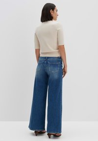 Beige, taillierter Kurzarm-Pullover kombiniert mit weit geschnittenen blauen Denim-Jeans. Die Jeans haben einen verblichenen Look und zwei Gesäßtaschen. High Heels runden das Outfit ab.