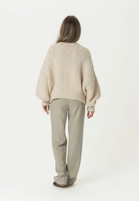 Chunky gestrickter beiger Pullover mit weiter Passform und geripptem Saum, kombiniert mit eleganten hellbeigen Hosen. Strukturierter Stoff mit Ballonärmeln.