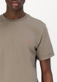 Kaki bombažna majica s posušenimi rokavi, ki ima na levi strani izvezeno oranžno "II" logotip. Gladka tekstura, priložnostna prileganje.
