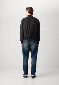 Schwarze Bomberjacke mit elastischen Bündchen, kombiniert mit blauen Jeans aus Denim mit leichtem Used-Look, getragen mit schwarzen Sneakern.