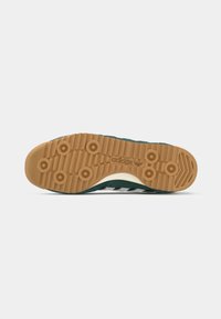 Green sneaker with a rubber gum sole, featuring textured grip patterns and three white stripes on the side, made from suede material.