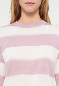 Pull en maille léger avec des rayures horizontales dans des teintes de rose pâle et de blanc, avec un col rond en côtes et une texture douce.