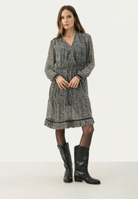 Rochie texturată alb-negru cu mâneci lungi, tiv ondulat și manșete contrastante, purtată împreună cu bocanci din piele neagră până la genunchi.