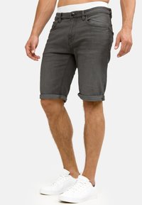 Shorts de mezclilla gris con dobladillos enrollados, diseño de cinco bolsillos y cierre de botón. Llevados con zapatillas blancas. Textura suave y forma ajustada.