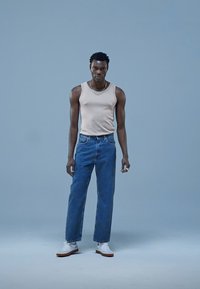 Beige linne, blå jeans i denim med rak skärning och vita sneakers. Enkel design, mjukt tyg och minimala detaljer.