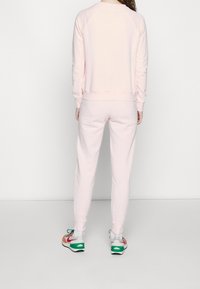 Rosa sweatshirt och matchande sweatpants, båda i ett mjukt bomullsmaterial. Har ribbade mudd och midja. Skorna har flerfärgade accenter.