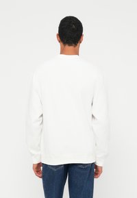 Λευκό φούτερ με στρογγυλή λαιμόκοψη από απαλό ύφασμα, με μακριά μανίκια και χαλαρή εφαρμογή. Λείος υφισμένος, χωρίς ορατά σχέδια ή γραφικά.