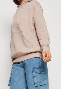 Felpa rosa chiaro con tasca frontale, cappuccio regolabile con cordini e polsi a coste, abbinata a pantaloni cargo blu con grandi tasche.