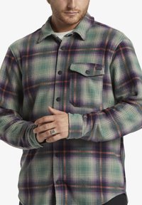 Geruit flanellen shirt in groene, paarse en oranje tinten; beschikt over een knoopsluiting aan de voorkant, een borstzak en een textuurstof met een zachte afwerking.