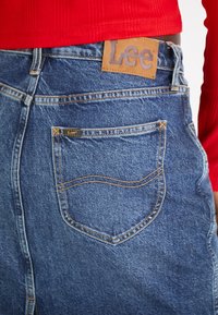 Niebieska spódnica dżinsowa z tylną kieszenią z zaokrąglonym przeszyciem, skórzaną łatką z logo Lee w kolorze brązowym oraz prostym krojem.