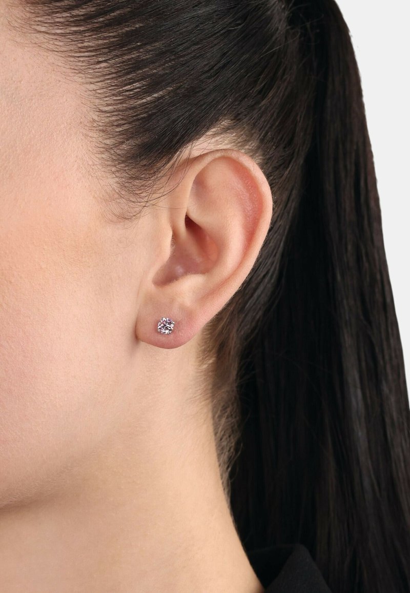 Pendientes de plata con un diseño minimalista que presentan una gema redonda y clara. Los pendientes se colocan cerca de la oreja, resaltando su diseño elegante.