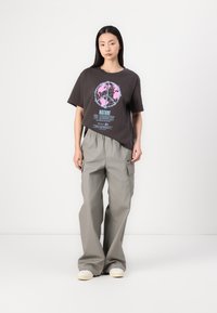 Mørkegrå T-shirt med et globusgrafik i pink og blå tekst, parret med løstsiddende, lys grå cargo-bukser og hvide sneakers.