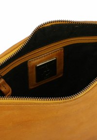 Interno di una borsa in pelle tan con rivestimento nero, caratterizzato da una cerniera metallica e un piccolo patch in pelle con logo impresso.