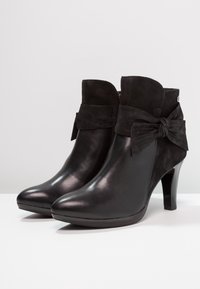 Černé kotníkové boty vyrobené z kůže a semiše s hladkým povrchem. Obsahují ozdobnou mašličku a zakrytý stiletto podpatek. Zapínání na zip po boku.