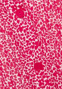 Camisa de botones rosa con un fondo crema, patrones de hojas en rosa y rojo, y dos botones rosas prominentes. Textura suave.