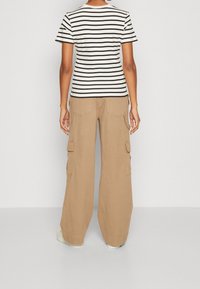 Krémové a černé pruhované tričko s krátkým rukávem je zkombinováno s béžovými širokými cargo kalhotami, které mají postranní kapsy a volný střih.